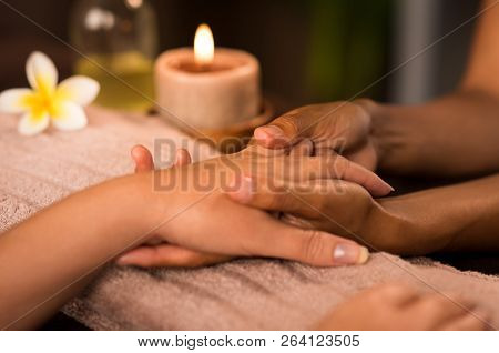 Closeup of woman getting manicure treatment in spa. Woman doing hand massage at wellness center. Detail of beautician hands doing massage hands to customer with candle on towel.