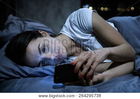 Smartphone Addiction. Young Tired Female Looking At Her Mobile Phone Screen, Lying In Bed Late At Ni