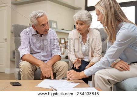 Business agent planning with a retired couple their future investment opportunities. Financial advisor talking to elderly man and woman and pointing the terms of contract on document. Retirement plans