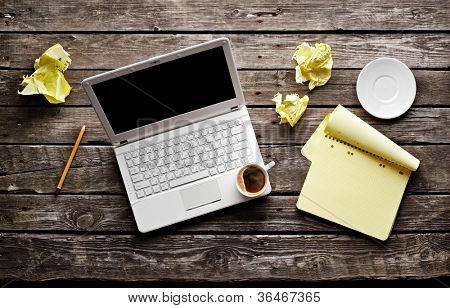 Laptop with crumpled paper, blank notepad and pencil on old wooden table. Workplace writer.