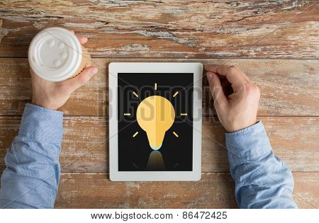 business, education, inspiration, people and technology concept - close up of male hands with lighting bulb icon on tablet pc computer screen and coffee cup at table