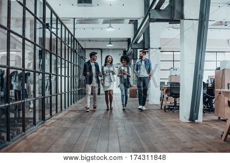 Young business professionals. Full length of young modern people in smart casual wear discussing business while walking through the office corridor