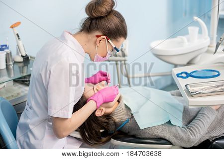 Female Dentist With Dental Tools - Mirror And Probe Treating Patient Teeth At Dental Clinic Office.