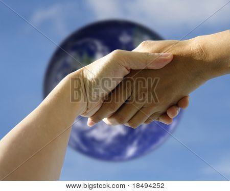 A pair of hands holding or shaking each other against a blurred earth. Concept: Agreeement reached or helping hand.