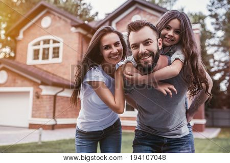 Happy family is standing near their modern house smiling and looking at camera.