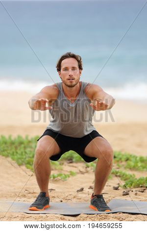 Squat exercise fitness man training squats for glutes and quadriceps muscles doing workout burpees working out beach in summer outdoors.