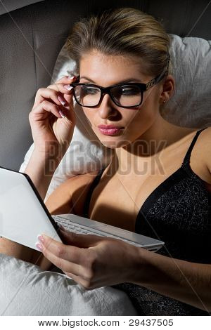 Portret van vrouw liggend op bed met een laptop