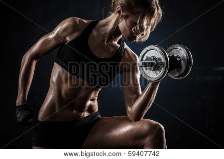 Brutal athletic woman pumping up muscules with dumbbells