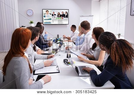 Group Of Businesspeople Having Video Conference With Another Business Team In Office