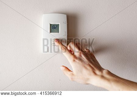 A Woman Is Pressing The Up Button Of A Wall Attached House Thermostat With Digital Display Showing T