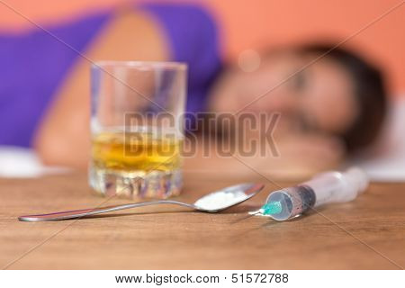 Drugs,syringe and alcohol with out of focus female addict on the background