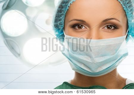 Young woman doctor in cap and face mask in surgery room interior