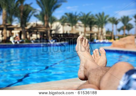 Sunbathing by the hotel tourist resort swimming pool, mans legs lying down on a sunlounger looking over the water