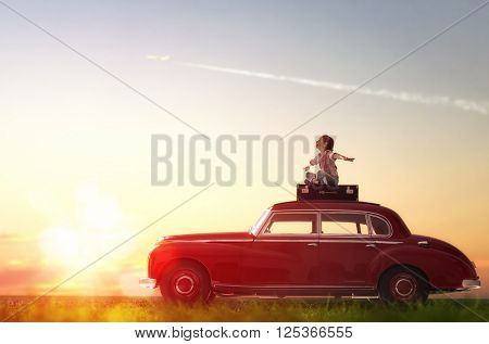 Toward adventure! Girl relaxing and enjoying road trip. Happy child girl sitting on roof of vintage car.