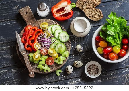 Fresh vegetables - tomatoes cucumbers peppers celery and garden herbs and spices on dark wooden background. Ingredients for fresh vegetable salad