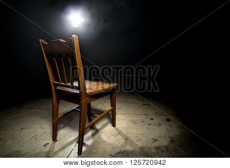 Isolated wooden chair in a dark scary prison with an interrogation spotlight