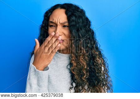 Young latin woman wearing casual clothes smelling something stinky and disgusting, intolerable smell, holding breath with fingers on nose. bad smell 