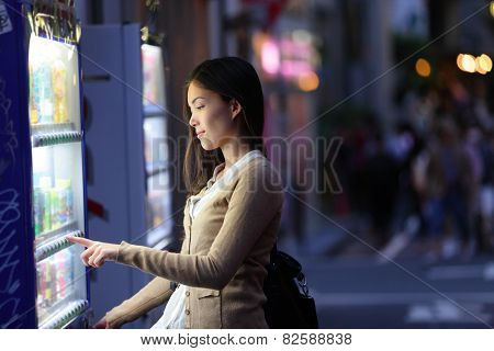 Japan vending machines - Tokyo woman buying drinks. Young student or female tourist choosing a snack or drink at vending machine at night in famous Harajuku district in Shibuya, Tokyo, Japan.