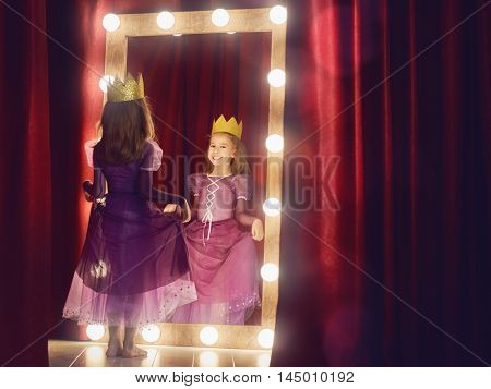 Cute little actress. Child girl in Princess costume on the background of theatrical scenes and mirrors.