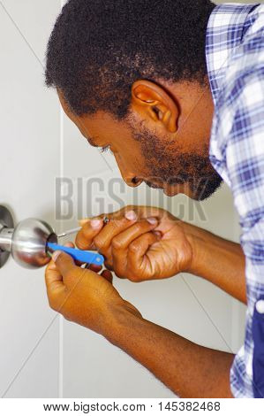 Closeup head and hands of locksmith using pick tools to open locked door.