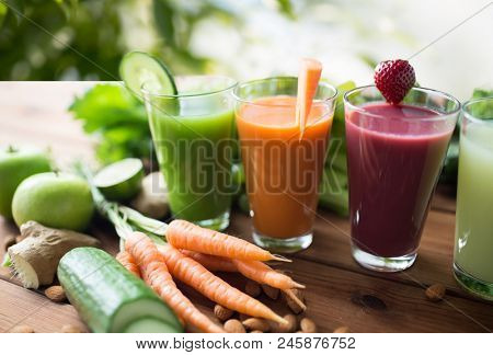 healthy eating, drinks, diet and detox concept - close up of glasses with different fruit or vegetable juices and food on table over green natural background