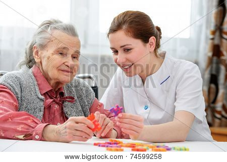 Elder care nurse playing jigsaw puzzle with senior woman in nursing home