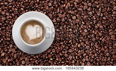 Top view - Coffee cup of LATTE ART Love symbol lover sign on top Pile of brown coffee beans with copy space for text or graphic design. Cafe' latte cream on top coffee in heart shape on background of raw coffee beans