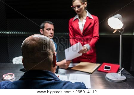 Rear view of a middle-aged suspect or witness sitting at desk during the police interrogation in front of the prosecutor and a female lawyer