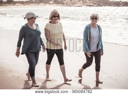 Lovely Group Of Three Active Senior Woman On Their 60s Walking, Exercising And Having Fun On The Bea