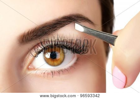 Young woman plucking eyebrows with tweezers close up