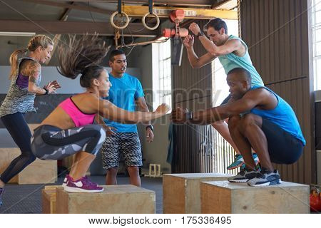 Instructor giving encouragement while fit strong healthy people do box jumps in fit gym