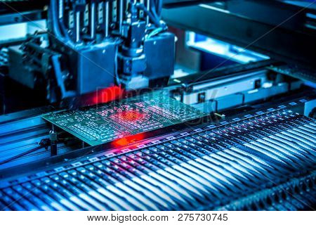 Electronic circuit under surface-mounting machine. Shot in red and blue tints. Surface-mount technology as a producing of electronic circuits. Components placed onto the surface of printed elements.