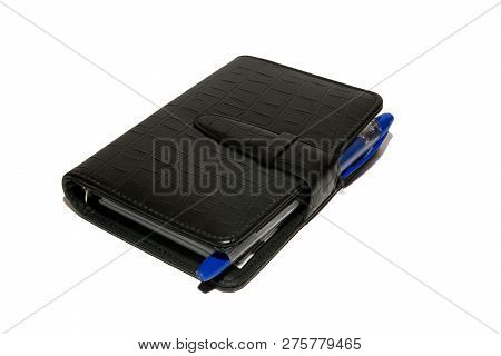 Black Diary With A Blue Ballpoint Pen Lies On A White Table. Diary And Pen On White Background. Isol