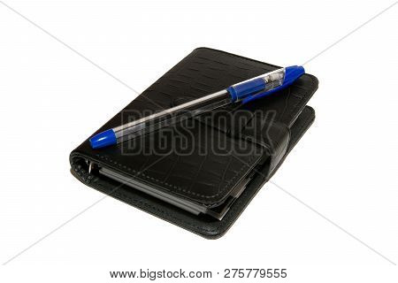 Black Diary With A Blue Ballpoint Pen Lies On A White Table. Diary And Pen On White Background. Isol