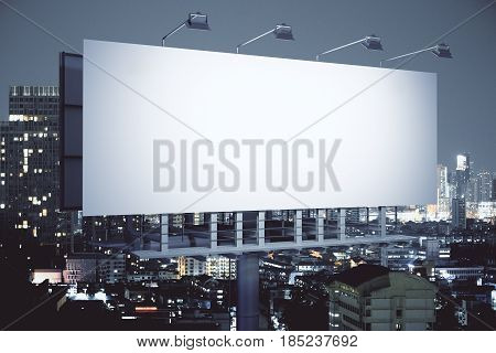 Side view of empty billboard on illuminated night city background. Advertisement concept. 3D Rendering