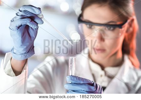 Life scientists researching in laboratory. Focused female life science professional pipetting solution into the glass cuvette. Lens focus on researcher's eyes. Healthcare and biotechnology concept.