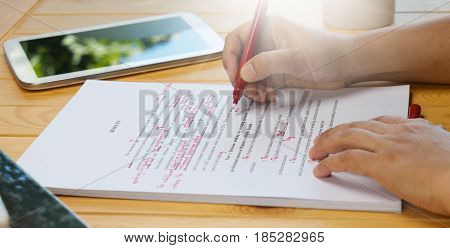 hand holding red pen over proofreading text on table