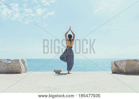 Young woman doing yoga in the beach. Female wearing sport clothes in eagle asana with defocused sea background. yoga beach. yoga vintage. yoga in sea. girl yoga relex. yoga fitness. yoga concept