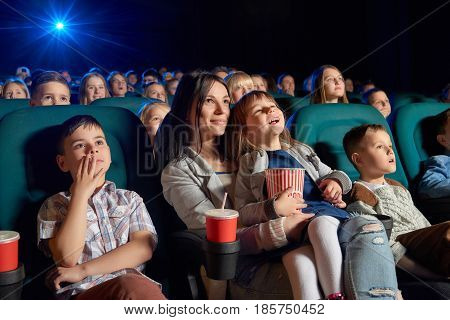 Low angle shot of people watching a movie at the cinema. Young woman and her daughter enjoying a film at the movie theatre motherhood parenting children kids entertaining happiness.