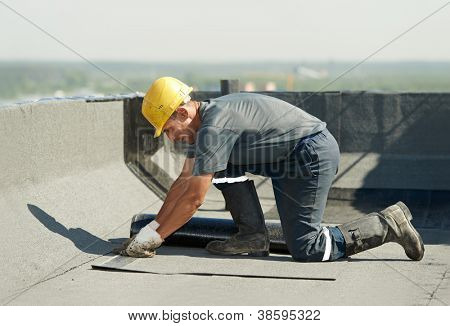 Roofer preparing part of bitumen roofing felt roll for melting by gas heater torch flame