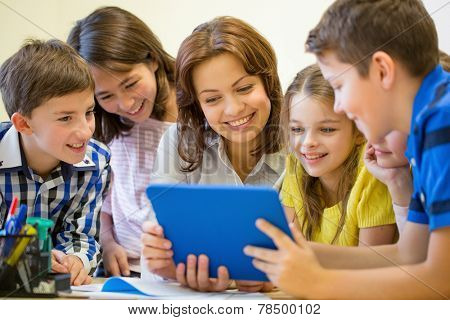 education, elementary school, learning, technology and people concept - group of school kids with teacher looking to tablet pc computer in classroom