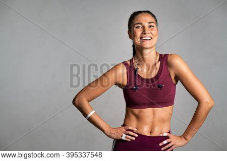 Portrait of beautiful fitness woman smiling and looking at camera isolated on grey background. Mid woman in sportswear relaxing after training at gym. Happy fit girl on gray wall with copy space.