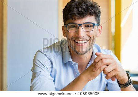 Closeup shot of young man wearing spectacle. Portrait of a guy with shirt and eyeglasses looking at camera indoor. Handsome smiling young man wearing blue spectacle.
