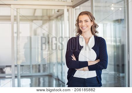 Portrait of mature beautiful business woman in the office looking at camera. Business executive standing in modern office with big smile. Cheerful mid businesswoman with copy space.