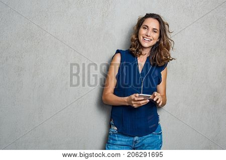 Smiling mature woman using smartphone and looking at camera. Happy woman typing on cellphone over gray background with copy space. Portrait of smiling latin woman messaging with smartphone. 