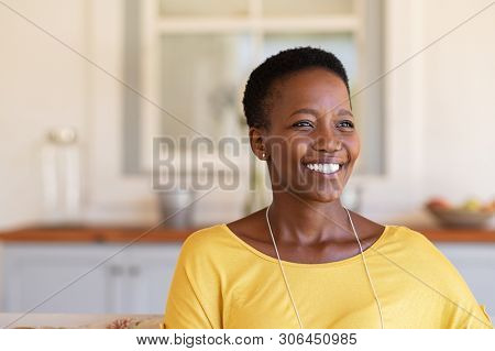 Mature black woman with short curly hair smiling and looking away. Closeup face of happy young woman relaxing at home under the patio. Beautiful carefree lady smiling with hope and copy space.