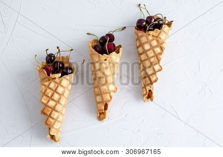 Ice Cream Cone Filled With Cherries On A Light White Concrete Background.