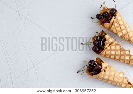 Ice Cream Cone Filled With Cherries On A Light White Concrete Background.