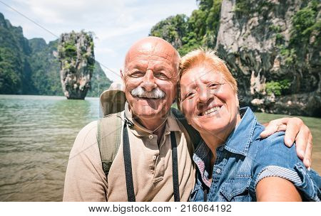 Happy retired senior couple taking travel selfie around world - Active elderly concept with people having fun together at James Bond Island in Thailand - Mature people lifestyle - Warm day filter