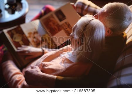 An elderly couple is considering a family photo album wrapped up in a plaid. Golden wedding, happy marriage, grow old together